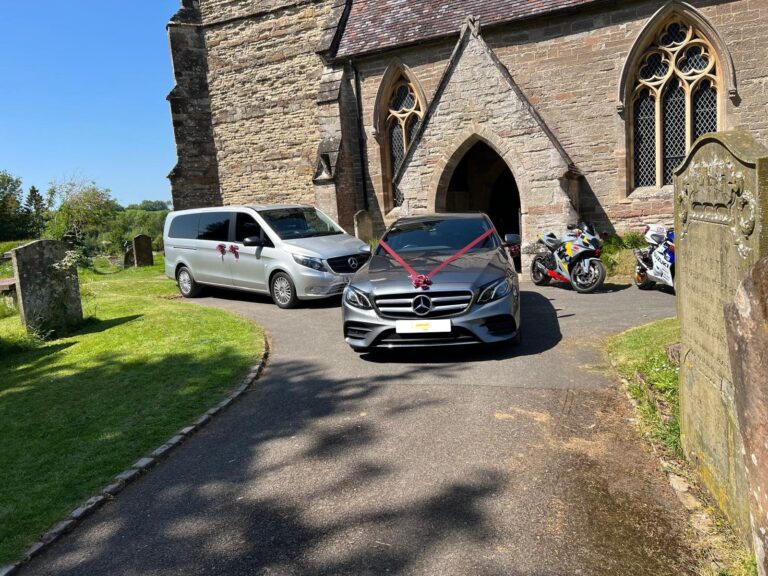 Mercedes E-Class wedding car with ribbon outside a church, with a Mercedes Vito for guests